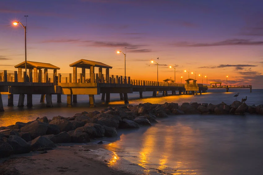 Serene view of the fishing pier at twilight in Fort De Soto Park, St. Petersburg, Florida. The soft evening light casts a peaceful glow over the pier as it stretches into calm waters, a favorite spot for anglers and nature enthusiasts.