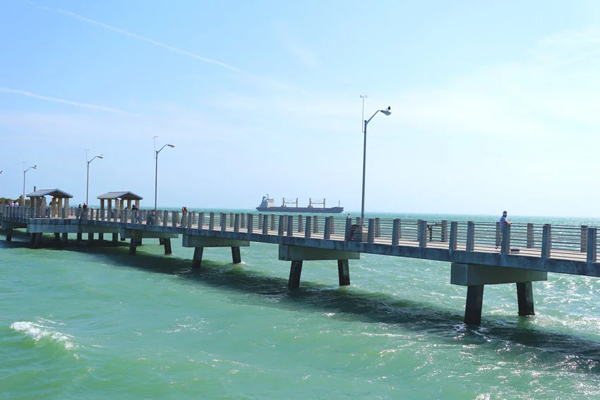 Scenic view of the fishing pier near Fort De Soto Park in St. Petersburg, Florida, U.S.A. The pier stretches into the calm waters, framed by lush greenery and the tranquil shoreline, providing an ideal spot for anglers and nature enthusiasts.