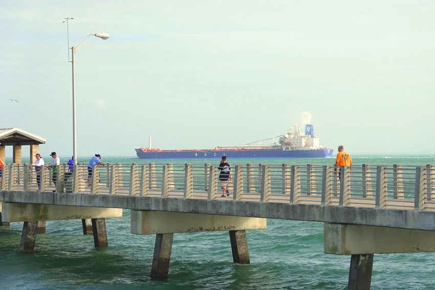 A large USCL container ship passing by the pier in St. Petersburg, Florida, sailing through calm waters with the surrounding landscape offering a striking contrast to the vessel's massive size.