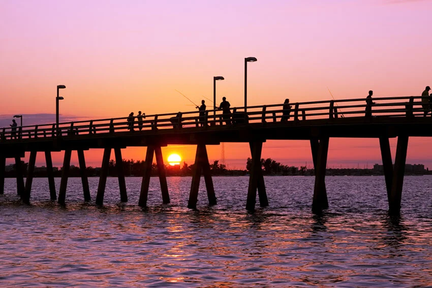Beautiful sunset view at the fishing pier in Florida. The vibrant hues of orange, pink, and purple fill the sky, reflecting off the calm waters as the pier stretches out into the horizon, creating a serene and picturesque coastal scene.