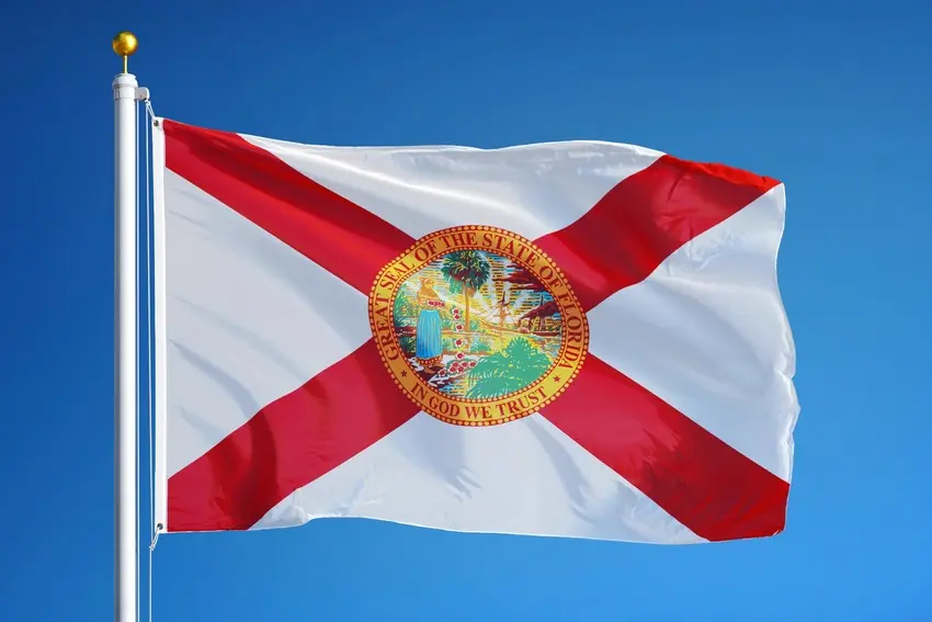 The Florida state flag waves against a clear blue sky, with its red diagonal cross and state seal visible.