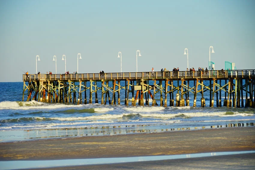 A side view of the fishing pier in Daytona Beach, extending over the calm ocean waters.