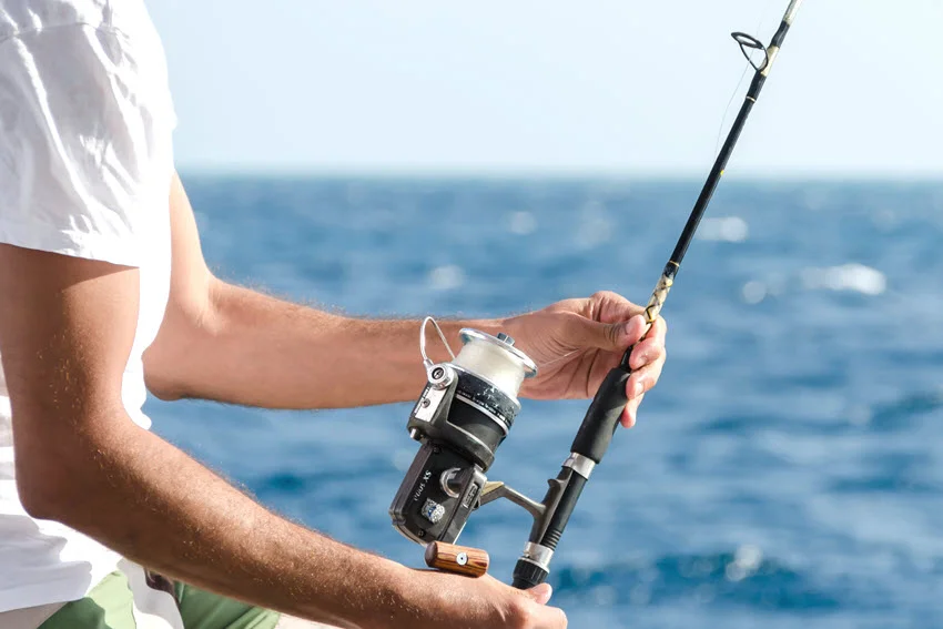 Close-up shot of an angler holding a spinning rod and reel over open water while preparing tackle for a Florida saltwater fishing trip.