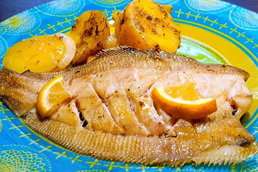 Close view of baked Flounder with onion, lemon, and potatoes, served on a blue and yellow plate.