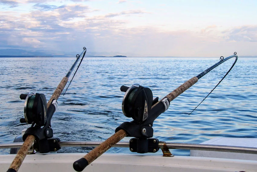 Two heavy action fishing rods attached to fishing boat fence against open ocean and sunset.