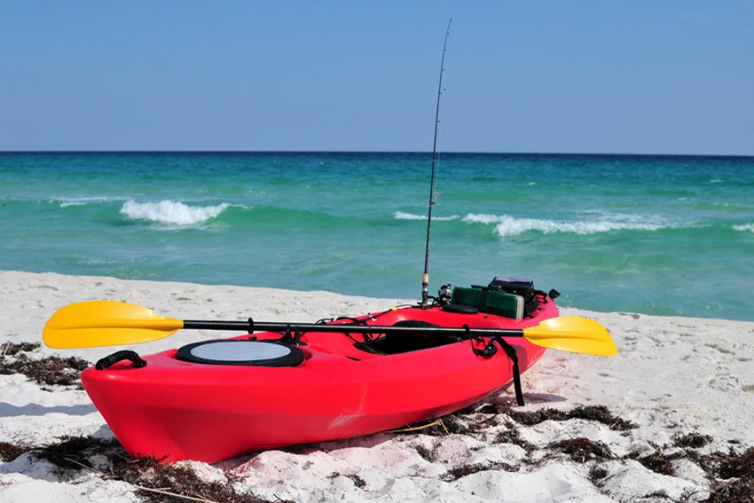A fishing kayak, equipped with gear, is positioned on the shore, ready for a day on the water.