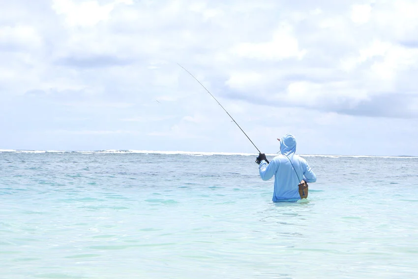 Angler standing in shallow, clear ocean water, up to his waist, performing sight fishing.