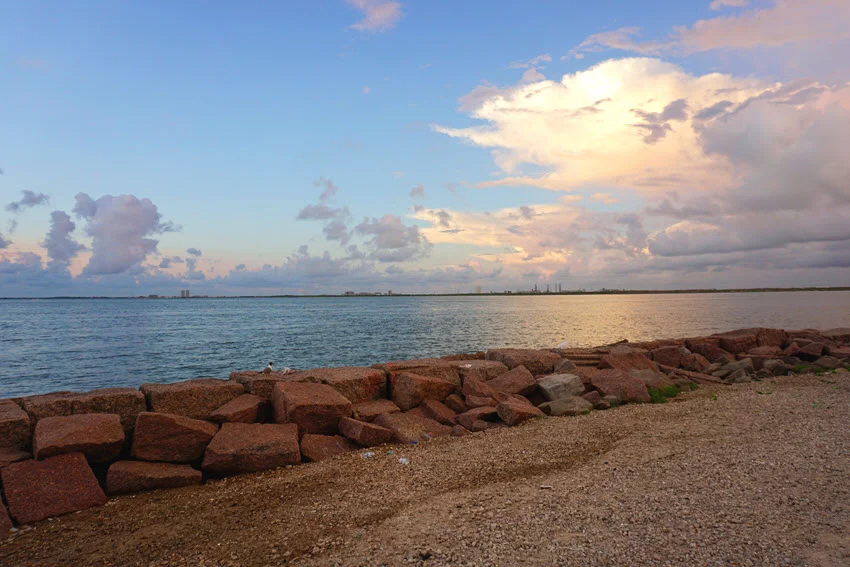 Panoramic view of East Bay waters, protective barrier, and gravel beach during sunrise.