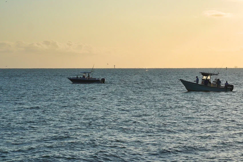 Two small fishing boats sailing in Galveston channel waters during sunset.