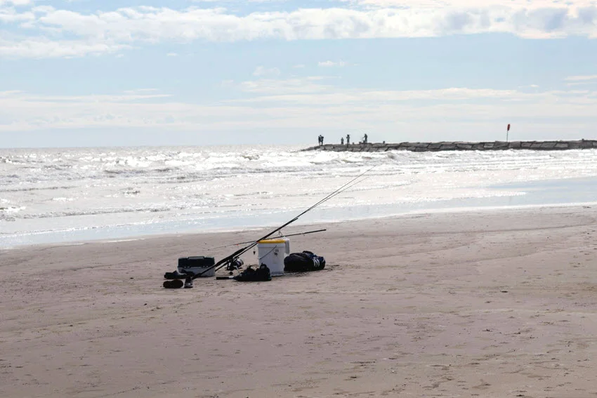 Panoramic view of the sandy beach in Galveston with fishing gear and a protective rocky barrier in the background.