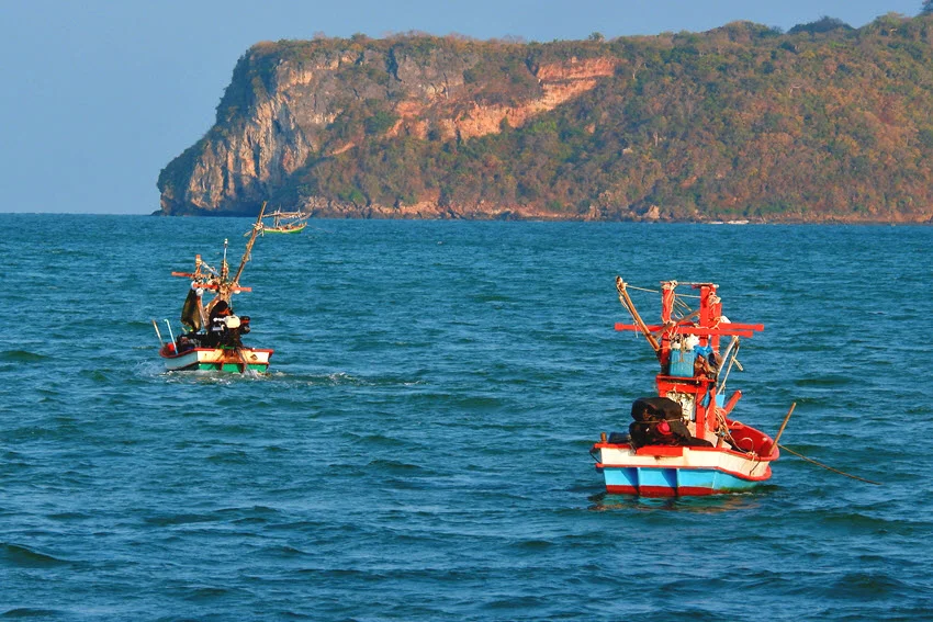 Distant view of two traditional fishing boats drifting on the restless ocean bay waters.