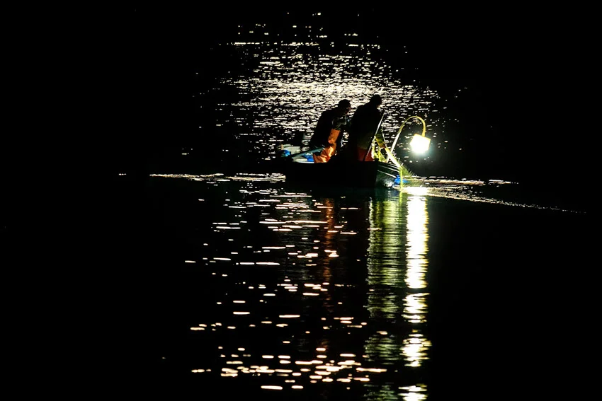 Anglers in a boat with lamps, during the night, on a lake, exploring water, searching for fish.