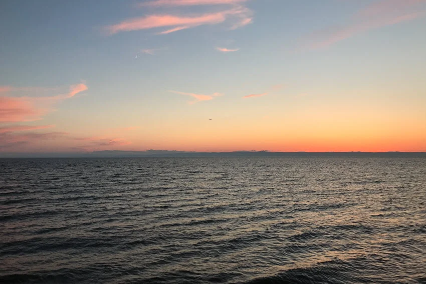  A view of a gentle-colored sunset casting soft hues of pink, orange, and lavender above the deep blue ocean.