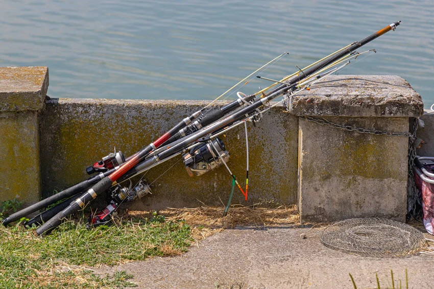 everal telescopic fishing poles placed close to concrete fence, close to the lake.