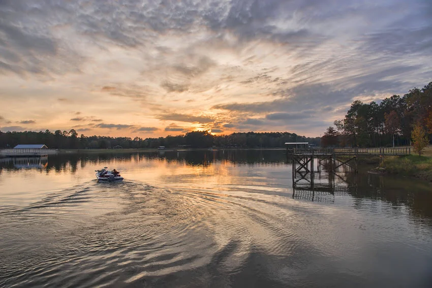 Boaters heading toward the sunset on Toledo Bend Lake, Louisiana, with vibrant orange and purple skies reflecting on the water.