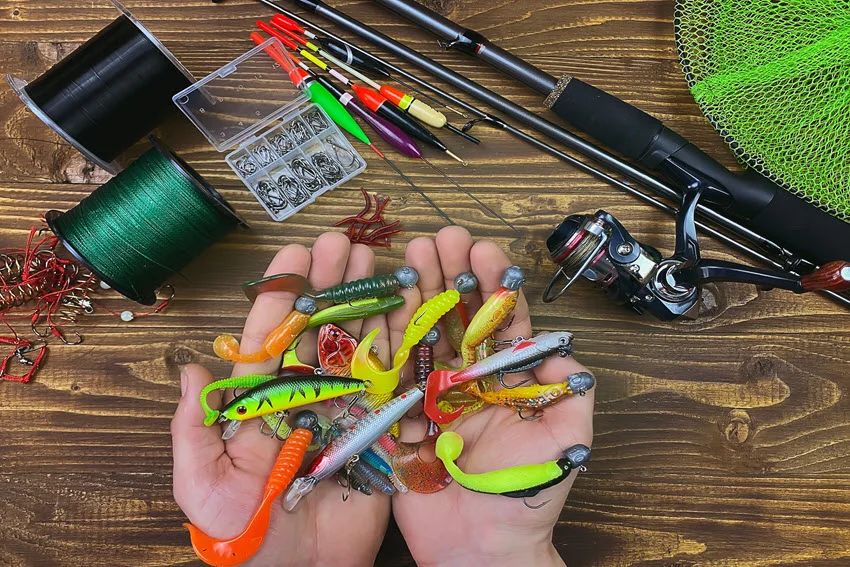 A variety of fishing tackle including a float, wobbler, and bait hooks laid out on a wooden background. The setup highlights essential gear for anglers, with selective focus drawing attention to the details.