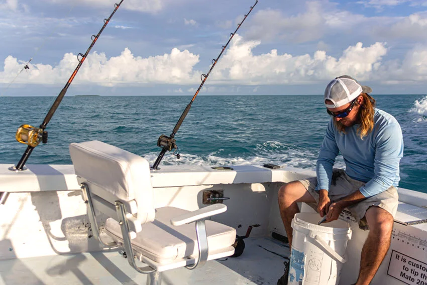 A saltwater angler prepares bait on a boat with trolling rods set up offshore, getting ready for Grouper fishing.