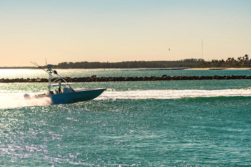 Center console fishing boat running through a Florida inlet near coastal structure and open water on a bright day.