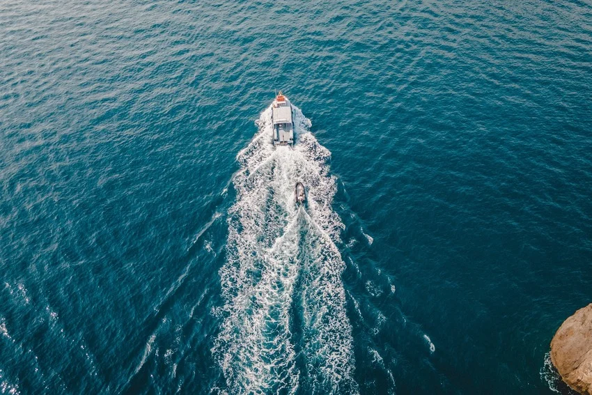 A motorboat travels through deep blue water, leaving a broad white wake beside a large partly visible rock.