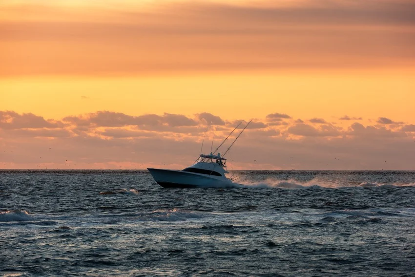 A sportfishing boat crosses open water at sunset, representing the changing seasonal conditions that shape fishing around Gulf Shores.