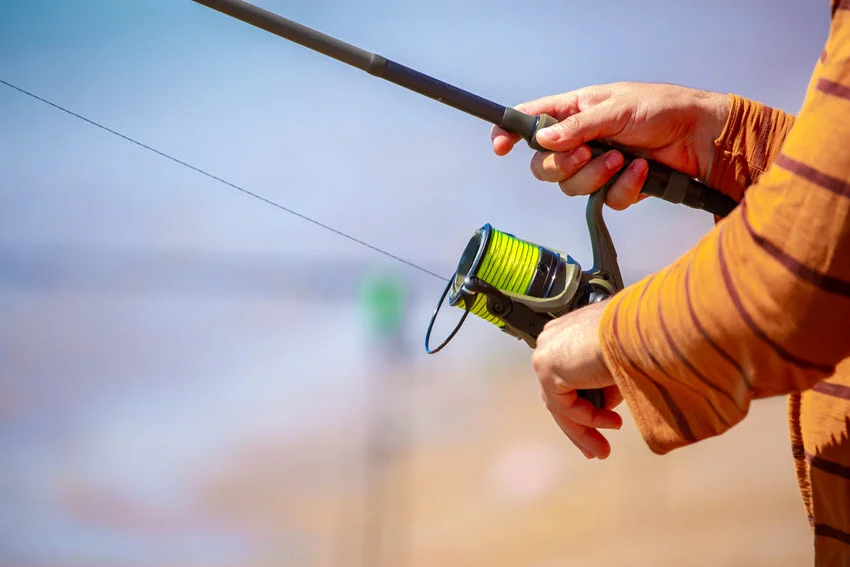 Focused shot of an angler's hands holding a fishing rod on an ocean shore.