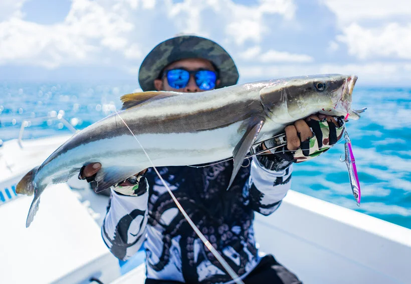 Happy angler posing with a freshly caught Cobia on open water during a sunny day.