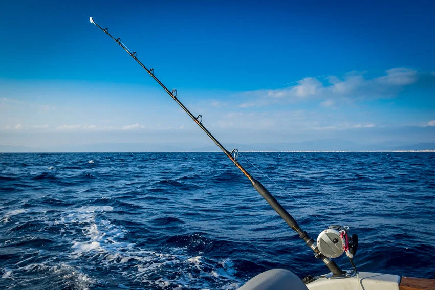 A sturdy trolling fishing rod secured to a moving boat, angled toward the water and ready for action.