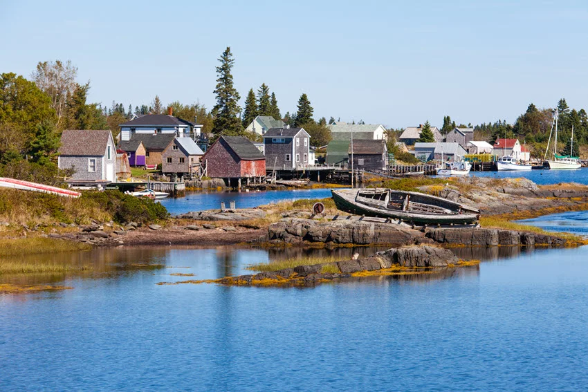 Blue Rocks fishing village in Nova Scotia, Canada, with wooden waterfront buildings, boats, and exposed coastal rocks beside sheltered blue water.