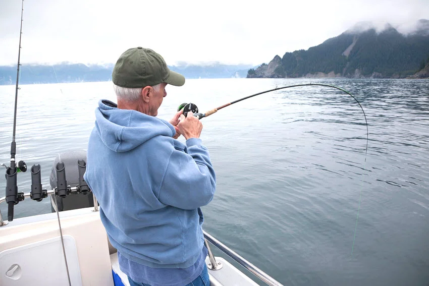 Angler fighting a fish from a boat near Seward, Alaska, illustrating the boat-fishing setting for chumming against a misty mountain coastline.