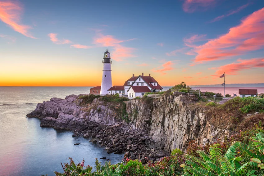 Portland Head Light in Cape Elizabeth, Maine, overlooking the rocky Atlantic coastline beneath pink clouds and a softly glowing sky.