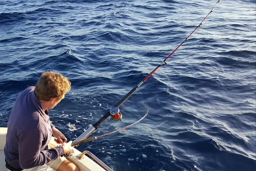 An angler works a fishing rod from a small boat on open water during a challenging day of fishing.