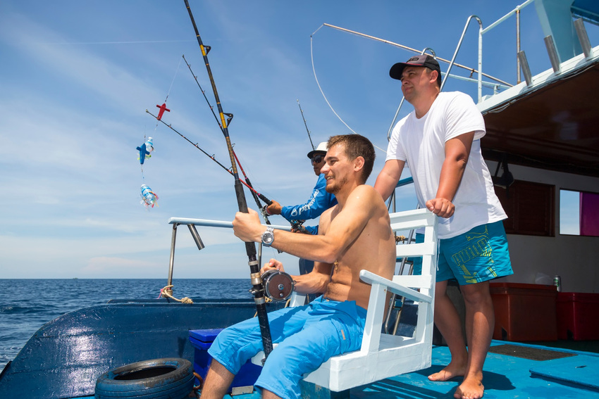 Three Anglers holding fishing rods aboard an ocean charter boat near Phuket, Thailand, with calm open water in the background.