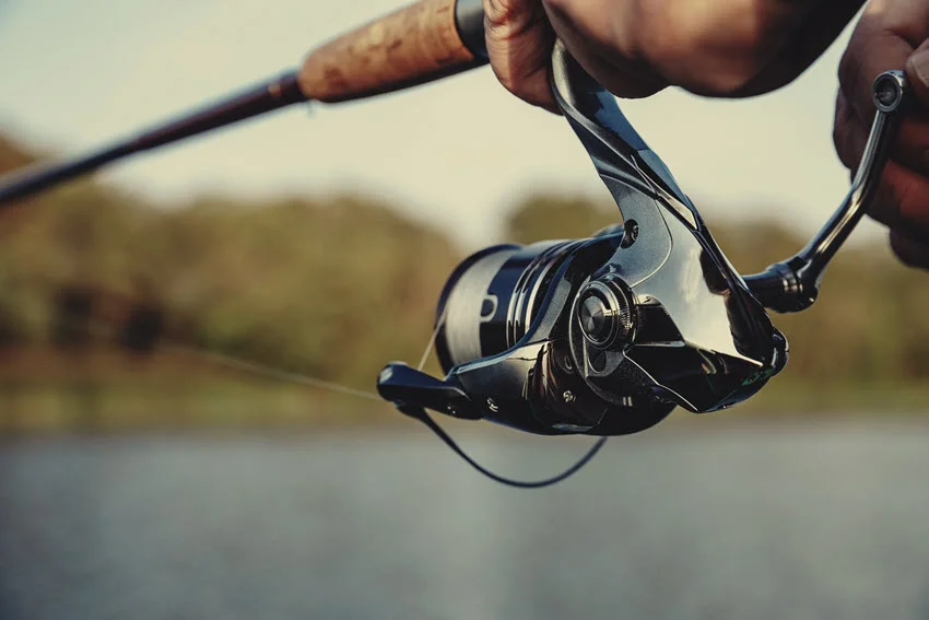 A person's hands holding a spinning rod with a spinning reel.