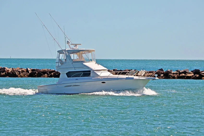 Close shot of a fishing boat with several fishing rods slowly cruising, with rocks nearby and the sea stretching to the horizon.