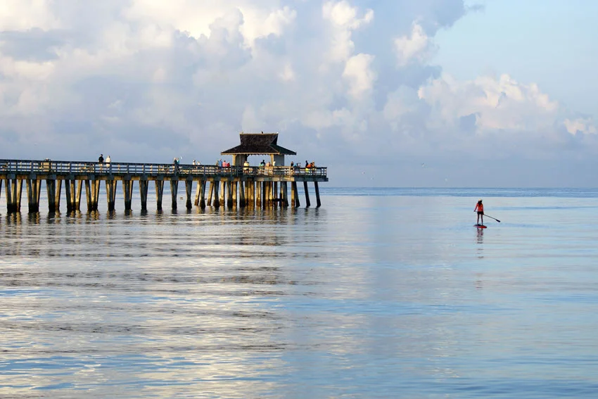 Angler on a paddle board, close to fishing pier, performs sight fishing.