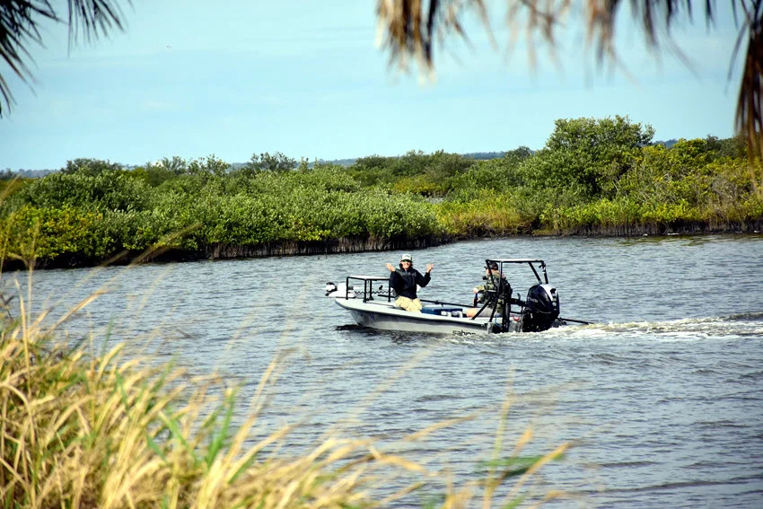 A lady on a small fishing boat sails down the estuaries water.