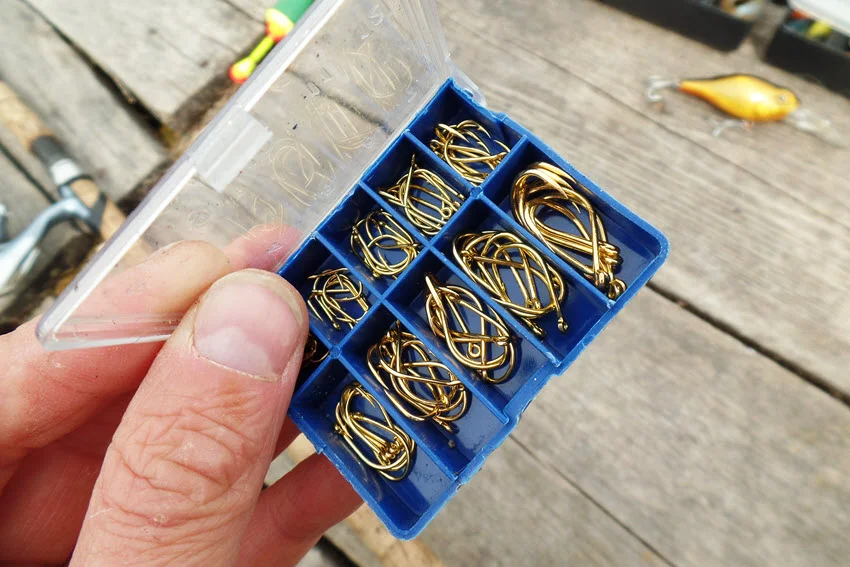 Close shot of an angler's hand holding a small blue fishing box filled with golden hooks.