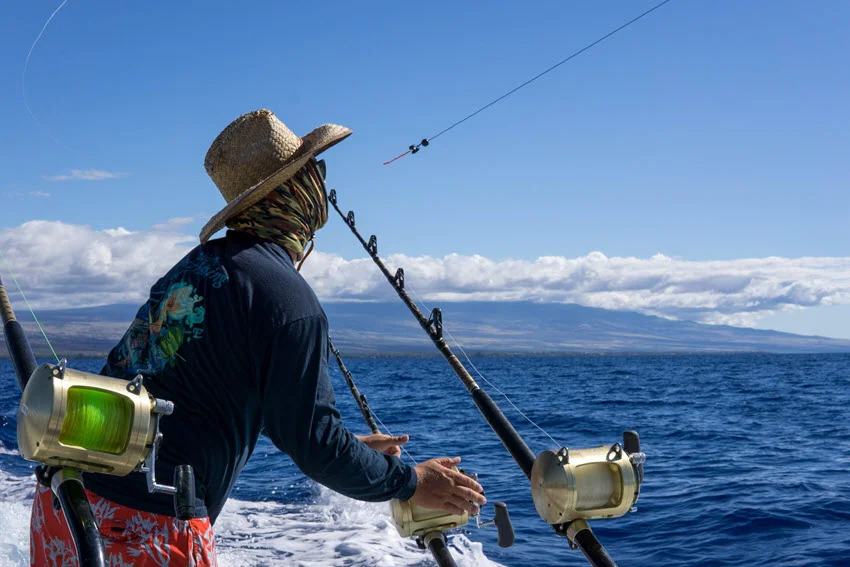 Side view of an angler on a moving boat handling the kite fishing rod, with the line extending over the ocean.