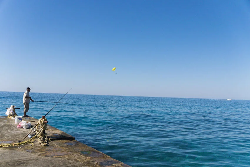 A view of an angler standing on a shore, performing kite fishing in the morning hours.