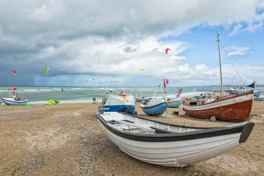 Fishing boats parked on the sandy beach, and several kite surfers were in the shallow, wavy water.