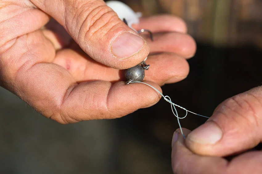 Close view of an angler’s hands preparing fishing rigs, attaching them to the line and hook with careful precision.
