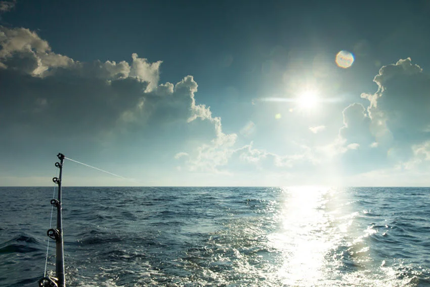 A fishing rod and kite line are attached to the moving boat on a cloudy day.
