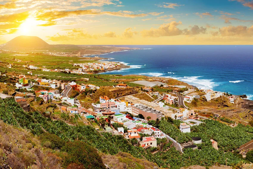 Sunset panorama of a coastal village in Tenerife, Canary Islands, Spain, with banana tree fields in the foreground and scenic beaches in the background.