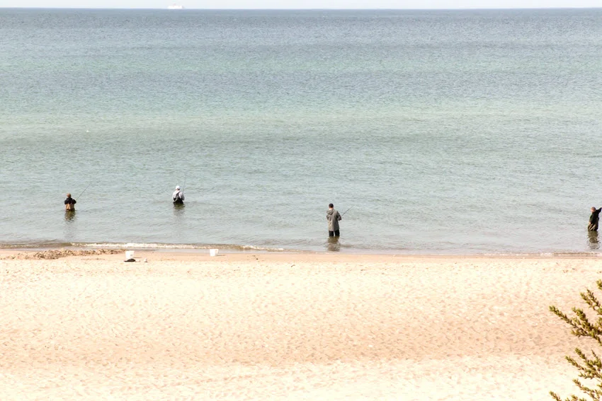 Anglers wading in shallow flats fishing waters near the sandy shoreline.