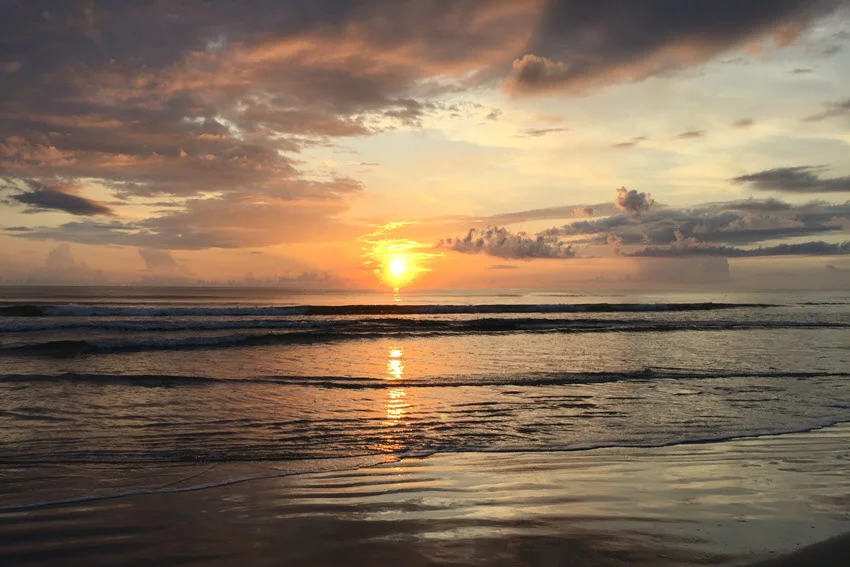 Sunrise view over the waves at New Smyrna Beach with colorful clouds reflecting on the water.