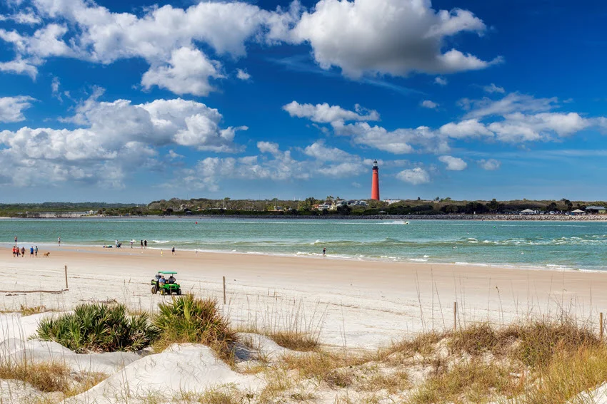 Scenic view of Ponce de Leon Inlet with sandy beach, turquoise water, and the red lighthouse in the distance.