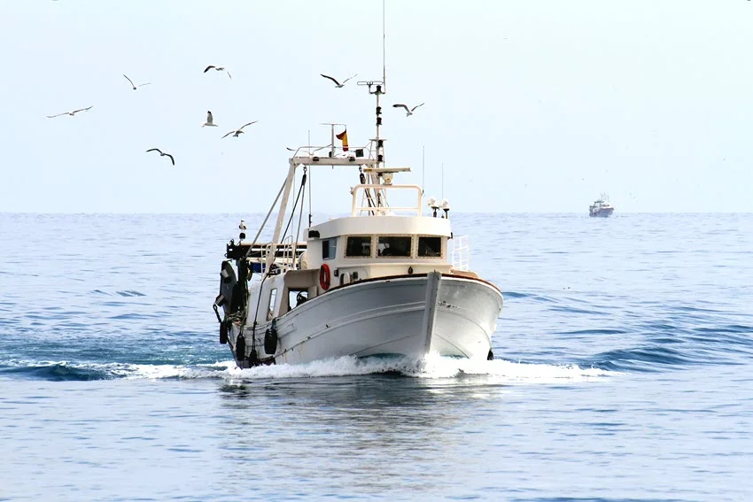 A focused shot of a fishing boat cruising across open water.