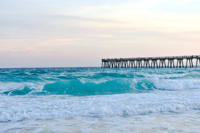 Navarre Beach Pier viewed from the shoreline, with ocean waves rolling beneath the structure under an open sky.