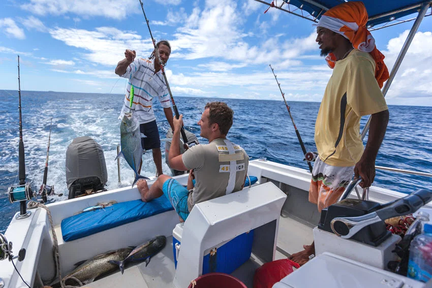 A back view of anglers on a trolling boat in action, with a freshly caught fish hanging from the hook.