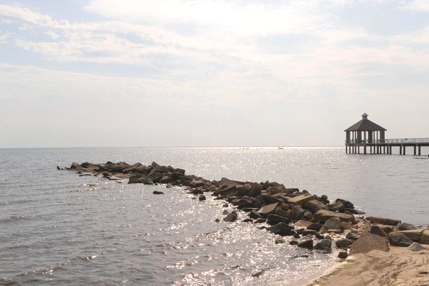 A panoramic shot of Lake Pontchartrain, with the wooden pier and rocky shore in sunset.